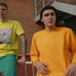 Two stylish young men in casual streetwear pose against an urban backdrop