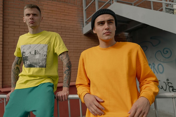 Two stylish young men in casual streetwear pose against an urban backdrop